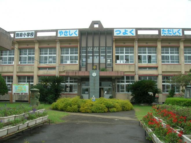 2階建ての校舎に「やさしく」「つよく」「ただしく」の言葉が掲示され、正面に時計台があり、きれいな花が植えられたプランターが校舎前に並んでいる南九州市立別府小学校の外観写真