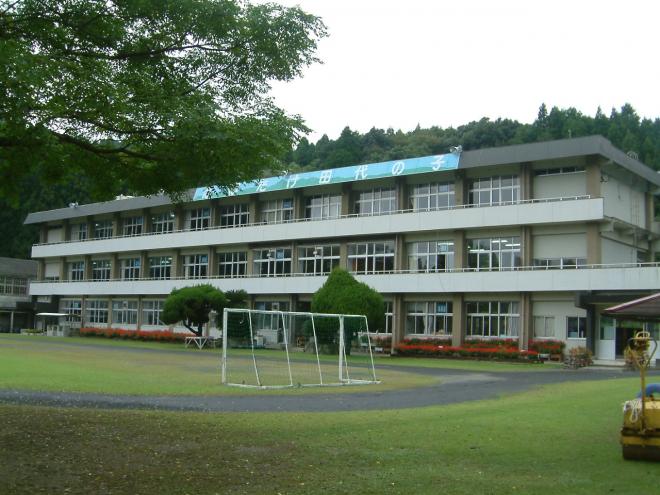 3階建ての校舎と校舎の前にサッカーゴールの設置された広い校庭がある旧田代小学校の外観写真