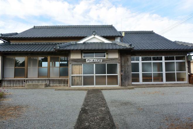 瓦屋根で中央の玄関の上に「門之浦公民館」と書かれた木の看板が取り付けられた、木造で、正面の全面がガラス戸の門之浦公民館の建物外観の写真