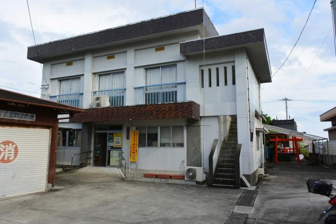 白を基調とした外壁の2階建ての建物で2階の窓には水色の柵が設置されており、2階へ上がる外階段がある大川公民館の外観写真