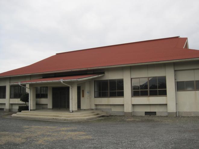 白壁に朱色の三角屋根で、3段ほどの階段の先に設けられている出入り口のスペースには屋根が設置されている南九州市頴娃武道館の写真