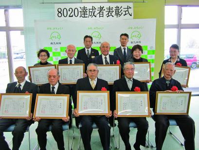 「8020達成者表彰式」と書かれた横断幕が掲げられた南九州市のバックボードの前で、胸に花をつけ額に入った表彰状を正面に向けて持った10名の男女が2列に並んでいる記念写真