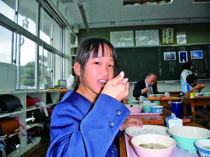 教室でトレーに乗った器から給食をうれしそうに食べている女子生徒の写真