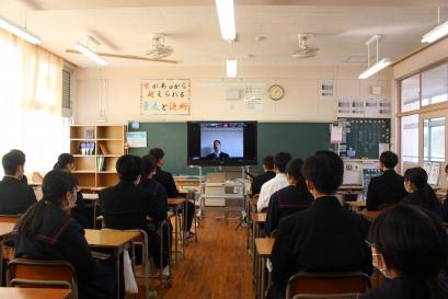 教室の黒板前に置かれたテレビ画面に横田さんが映し出され、その画面を、席に着いた生徒たちが姿勢を正して見ている様子の写真