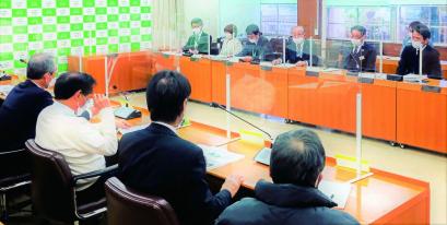 アクリルボードが設置された2人掛けの会議机が4台ずつ向かい合って配置され、それぞれの席に参加者が着席している写真