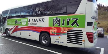 白い車体に、若草色の背景に大きく黒い字で肉バスと書かれた大型バスが駐車場に停まっている写真