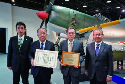 旧陸軍四式戦闘機「疾風」の前に4名の男性が並び、中央の塗木市長ともう1名は認定証を持っている写真