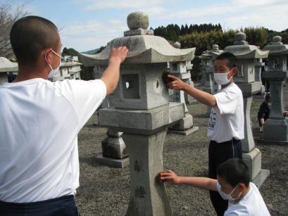たくさん並んだ石灯籠の一つを3人の生徒がたわしなどで磨いている写真