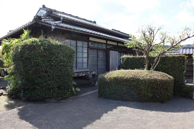 瓦屋根の平屋で、敷地内に木や生垣がある平山邸の写真