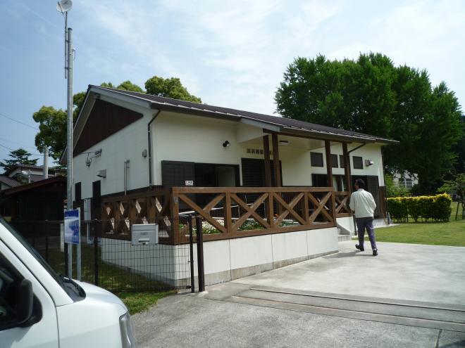 大きな木がある芝生の広場の一角に建ち、入り口左側にスロープが設置されている大丸地区公民館の外観写真
