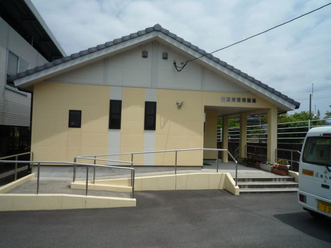 入り口へ続く短い階段と長い手すり付きのスロープがある、薄黄色の壁にグレーの瓦屋根の川辺地区公民館の外観写真
